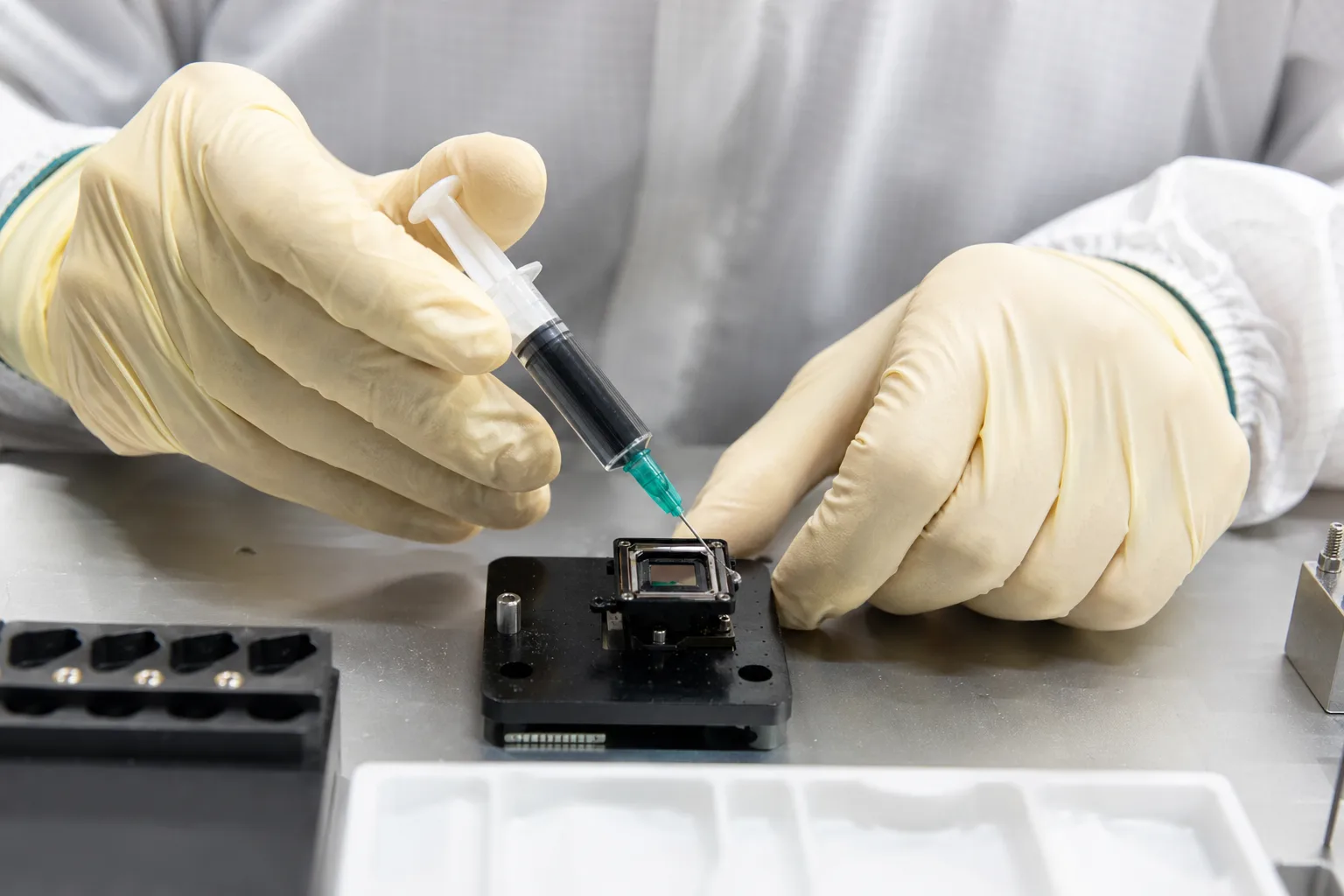 A technician uses industrial tools to carefully apply a soft encapsulant to a MEMS sensor, which illustrates the attention required for minimizing mechanical stress.