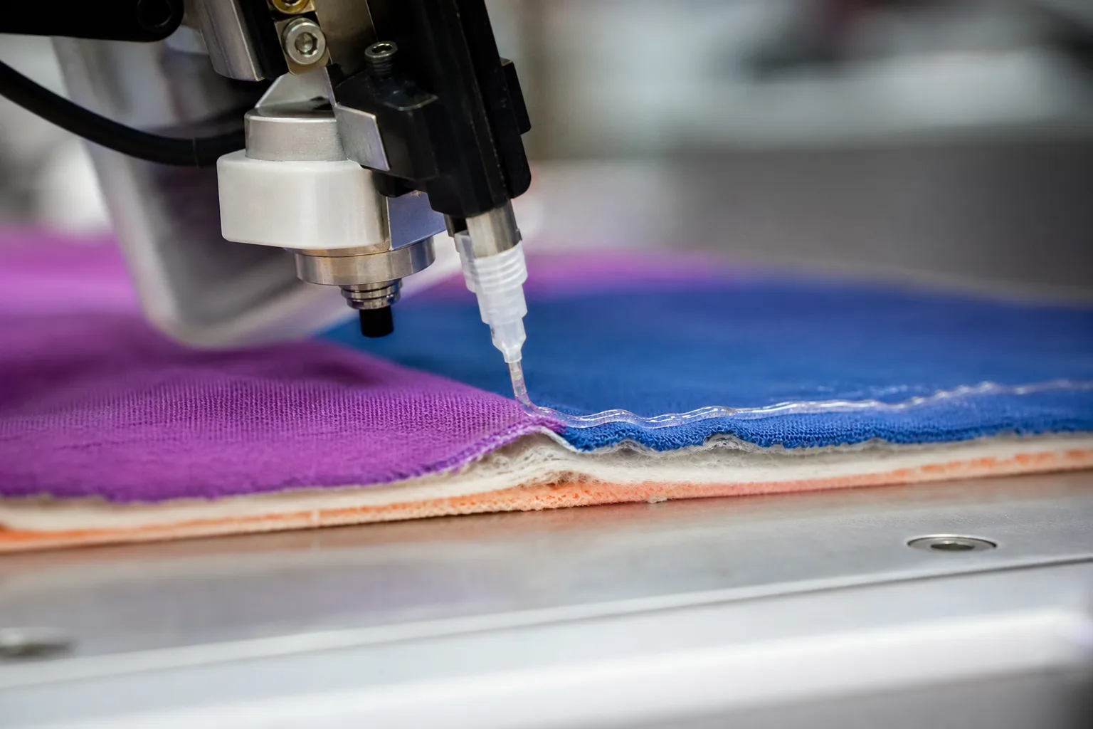 A detailed view highlighting flexible instant adhesives for soft materials being precisely dispensed onto delicate fabrics, illustrating industrial production processes.