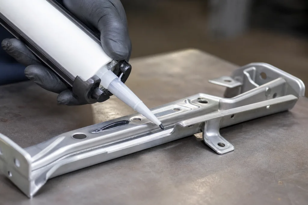 Operator dispensing industrial adhesive onto a metal automotive bracket with a cartridge gun